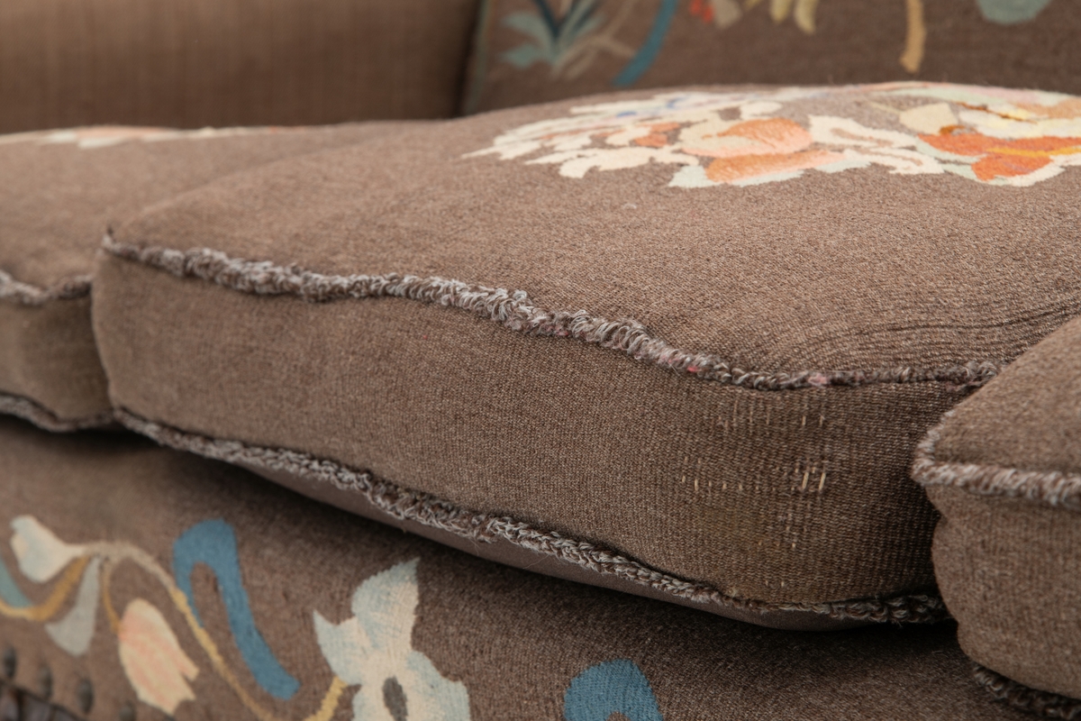 Sofa med trekk vevd av Ulrikke Greve. Vevnaden er vevet spesielt til denne sofaen. Det  er nyere stoff-trekk på armlenene. Møbeltrekket er nå stiftet fast med stiftemaskin; antagelig en reparasjon, og dekorert med pyntestift i messing.