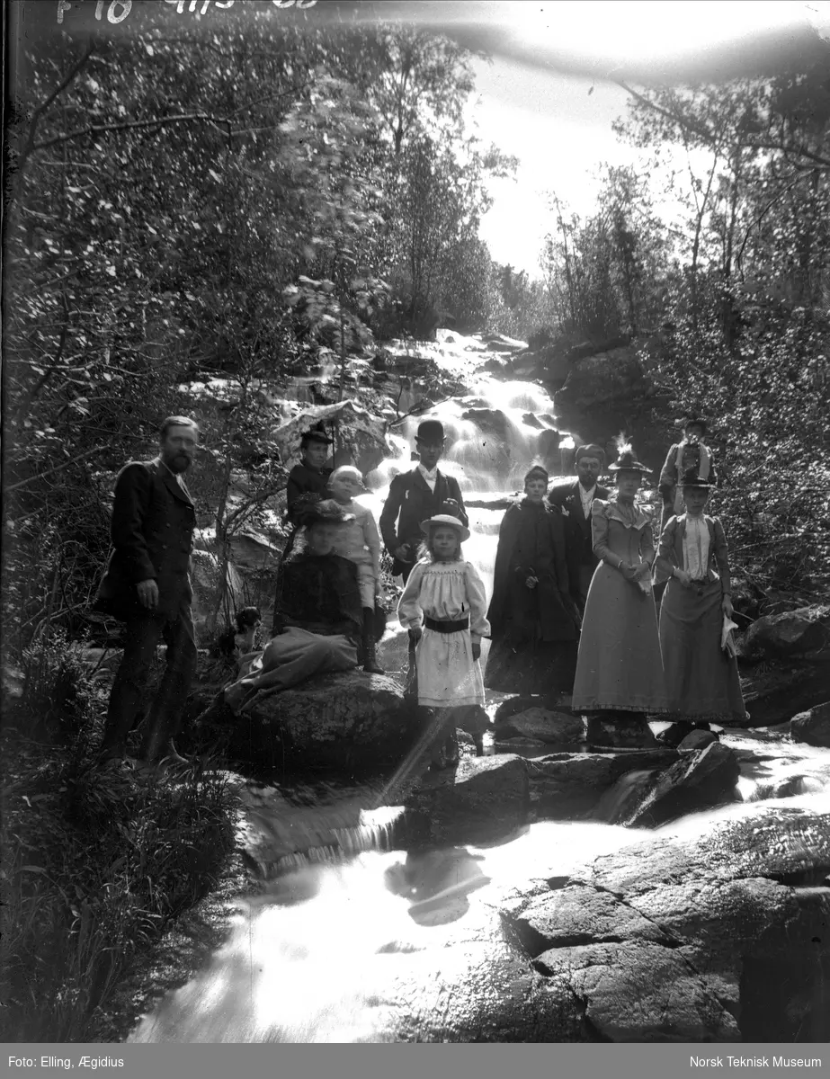 Ægidius Ellings familie på tur : fotografert oppstilt i en elv med foss i bakgrunnen