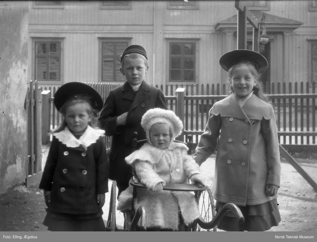 Barn, tre piker og en gutt i sin fineste utestas fotografert i haven oppstilt foran stakittgjerde : muligens Ægidius Ellings døtre i forgrunnen