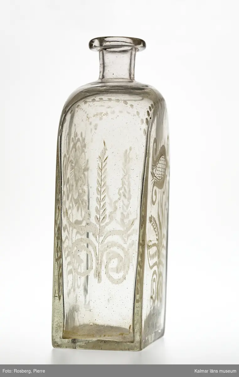 KLM 13688. Flaska, brännvinsflaska. Av glas. Fyrsidig. Graverad dekor på alla sidor i form av blommor och sädesax.