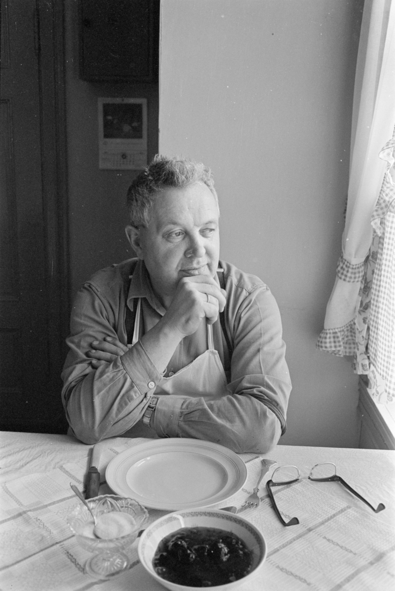 En mann sitter ved et dekket kjøkkenbord.