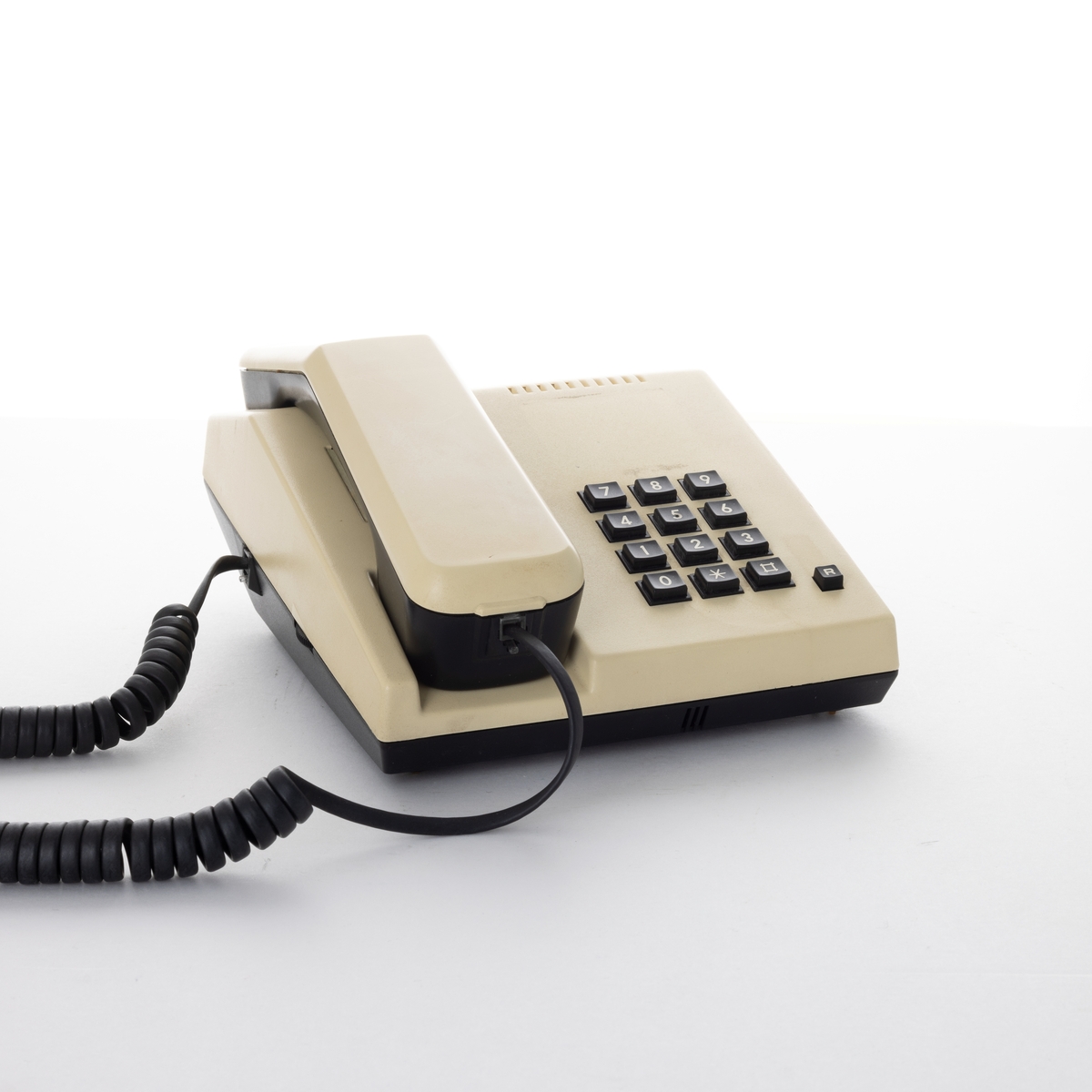 Kremfarget og svart telefon med svarte taster og svarte ledninger