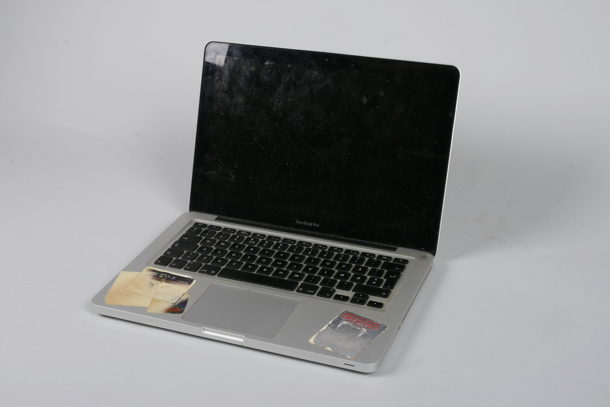 Bærbar datamaskin av typen Macbook. Kledd i metallmateriale. Kan åpne med hengsler på den ene langsiden. Innvendig skjerm og tastatur.