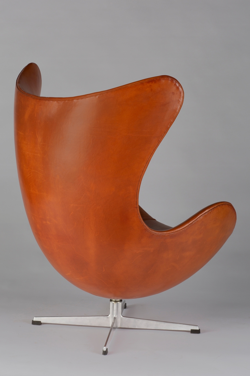 Skulpturell lenestol med myke, organiske linjer. Stolen har en indre kjerne av polyuretan med glassfiberforsterkning, som er dekket med kaldskum og trukket i lys okseskinn. Den nedre delen består av en mattpolert dreibar midtdel av stålrør med firestjernersfot i aluminium. Lenestolen kan dreies 360 grader.