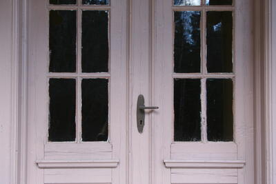 Skinnarbøl skolemuseum. Nærbilde av inngangsdøren. Døren ser lyserosa ut på fotografiet. Det er en dobbeltdør. Det er vinduer med spiler i døren.