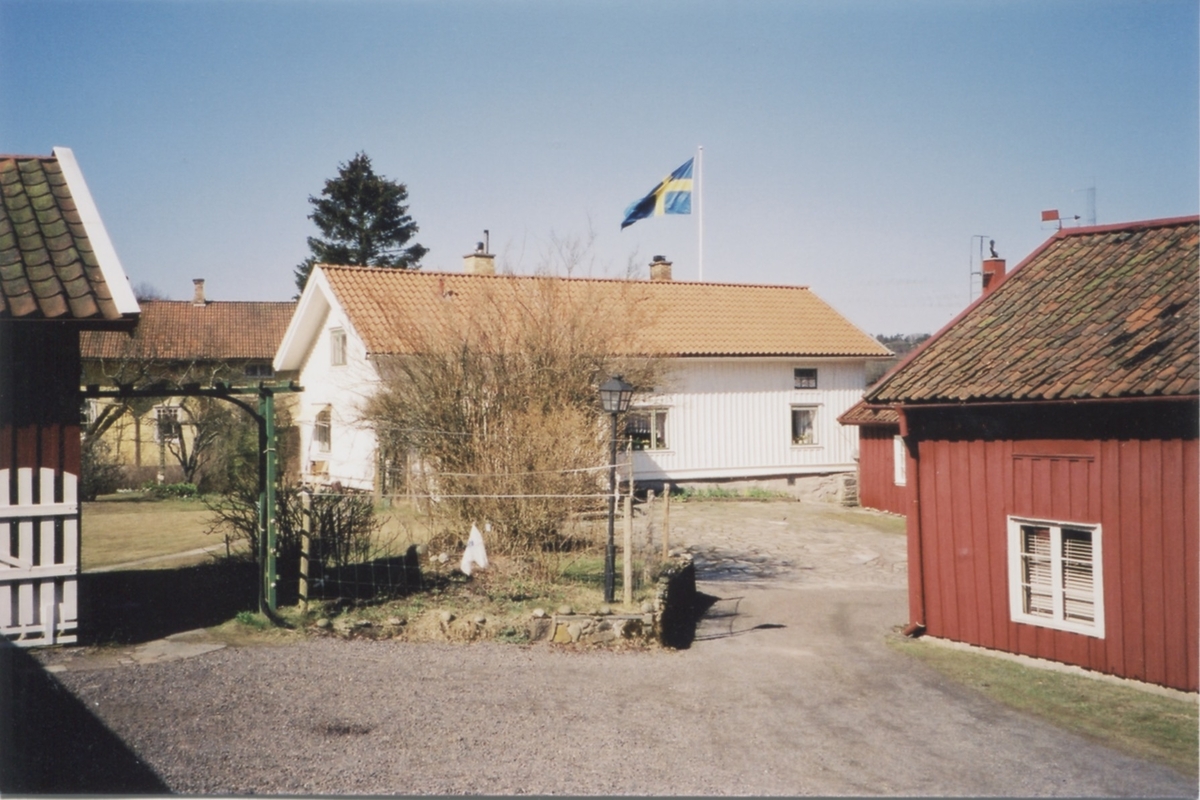 Två gårdar i Heljered 1980-tal. Främst ses Erikssons Heljered Mellangård 1:2 "Store Börjes". I bakgrunden till vänster skymtar det gula huset Heljered Västergård 3:3 "Larses Johns". Svenska flaggan är hissad.