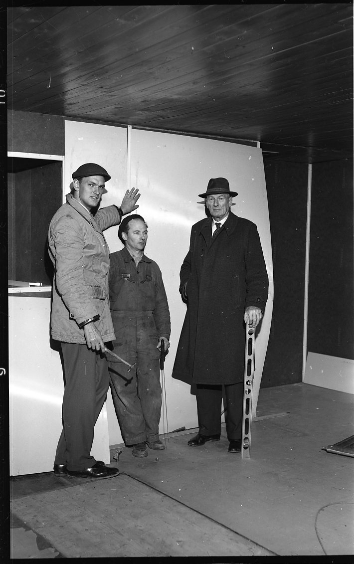 Tre män står i ett rum som sannolikt är under reparation. Från vänster Rolf von Otter med en hammare i handen, gårdskarlen Alf Lago i overall samt Rolf Gyllensvaan i hatt, rock och med ett vattenpass i handen.