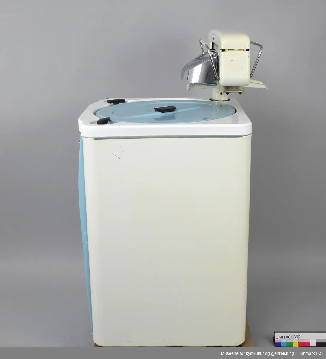 Denne vaskemaskinen er av emaljert metall, har avrundede kanter og en frontdør og lokk i blå lakkert metall. Maskinen har en bryter og en driftslys foran. 
Maskinen har en tilhørende elektrisk vrider (GMH.00891) som er festet på toppen. Vaskemaskinen er en såkalt "Agitatormaskin". Det betyr at den har en skovl i bunnen som beveger seg frem og tilbake i vaskeprosessen. Maskinen har et varmeelement og en elektrisk vannpumpe, samt fire hjul under. Hjulene er ikke montert. 
Oppå maskinen er en hendel som er merket: PUMPE PÅ-AV og hendel merket: TREKK OPP FOR START VASK. Den hvite bryteren foran er merket: I, II og III. På hjulene står det: FLEXELLO/MADE IN ENGLAND. Bak på døra er det skilt med følgende påskrifter: MÅ BARE TILKOBLES JORDINGSKONTAKT / 16 M 195299 MANUFACTURED BY WILKIN & MITCHELL LTD/ DARLASTON.S.SAFF. ENGLAND / Type E Volt 220. 
Med maskinen følger det en bruksanvisning, en vaskeklype (GMH.000894) og en gummislange (GMH.000893). Pakningen er porøs og det er 5 deler avbrudd som følger med separat.