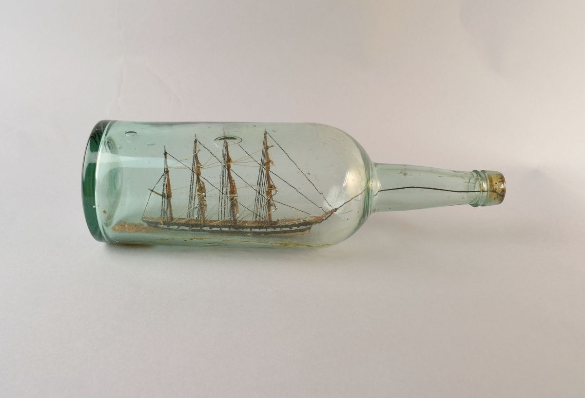 Modell av firemastet skip uten seil inni flaske.