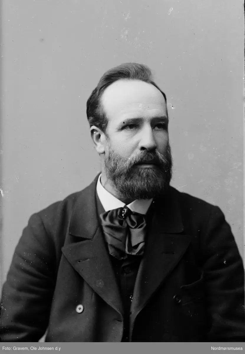 Portrett i halvfigur av mann med dress og skjegg. 