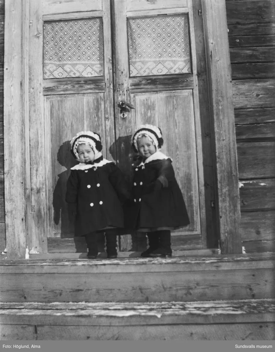 Fotografens tvillingdöttrar Irma och Ingrid Höglund på en trapp framför dubbeldörrar.