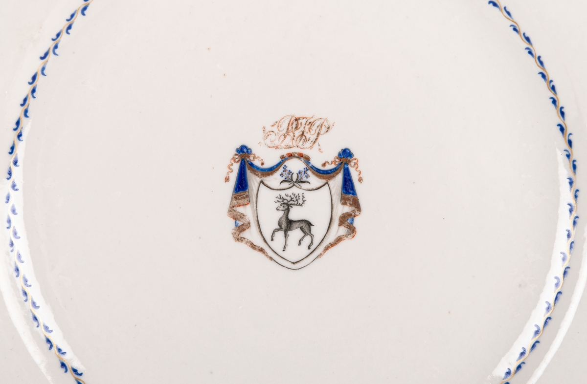 Flat tallrik tillhörande servis i porslin, Ostindien, 19 delar. Gråblå glasyr, bård av små förgyllda eklöv på mörkblå botten. Gestriklands vapen och monogram: R. F. P = Robert Fredrik Petre.