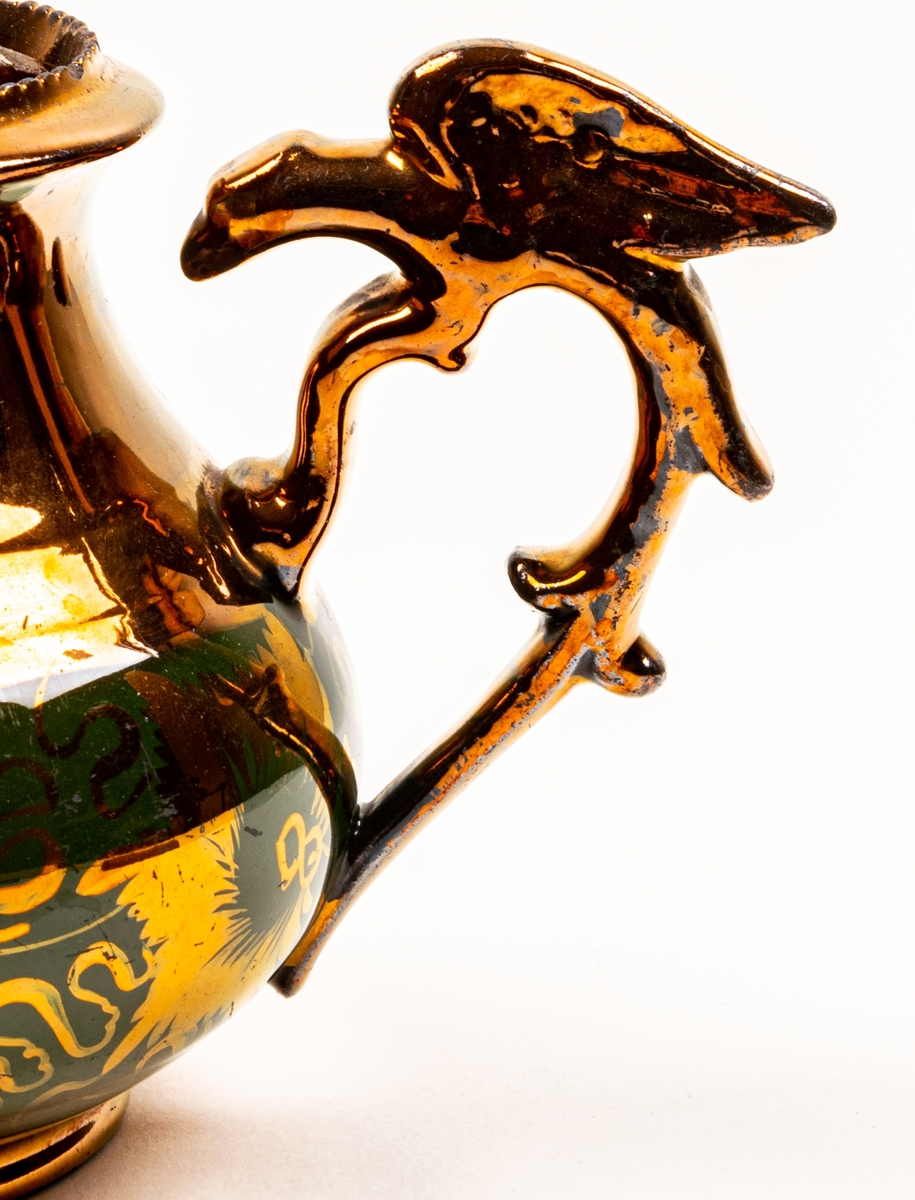 Tekanna, keramik, glasyr övervägande i starkt kopparglänsande färg, med bård av grönaktiga blomster nertill.