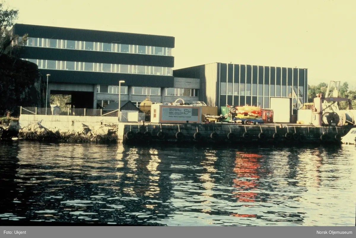 NUI, senere NUTEC utenfor Bergen, sett fra sjøsiden. På kaien står diverse utstyr, som konteinere, dykkerkammer og wirere.