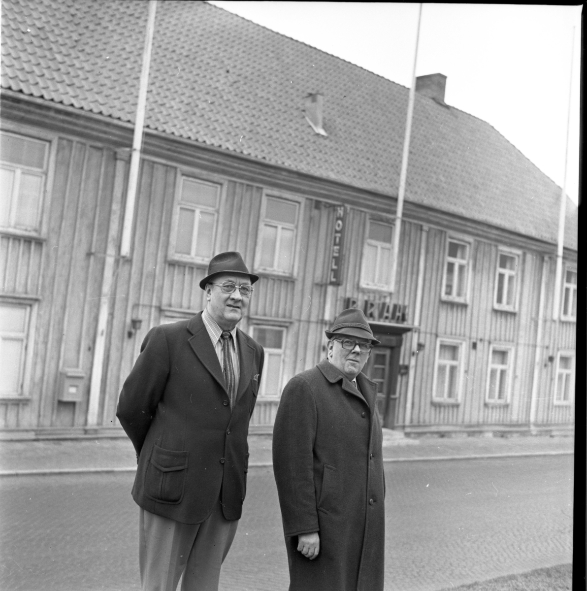 Två män med hatt står vid Brahegatan i Gränna framför Hotell Brahe.