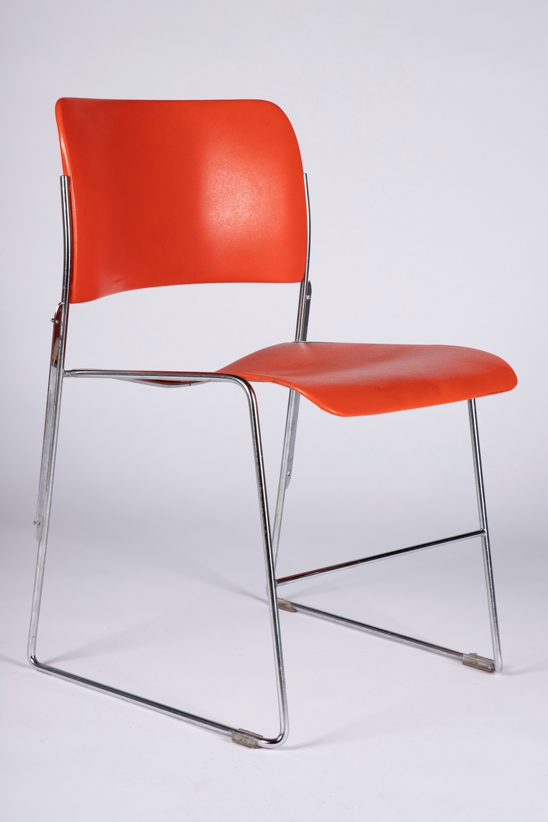 Stol med ramme i forkrommet metall og med åpen rygg. Sete og rygg i støpt plast. Stolen kan stables. Understellet står på fire plastknotter.