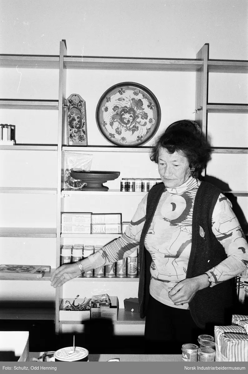 Kvinne ved butikken på Frøystul. Mange varer ligger i hyllene, blant annet skismørning og et rosemalt fat.