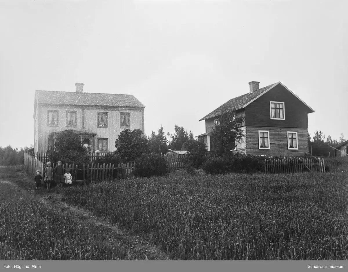 Två vyer mot gården Jöns Ols i Gräfte med två bostadshus och trädgården inhägnad med spjälstaket. Fyra barn, två kvinnor och två män syns på bilderna.
