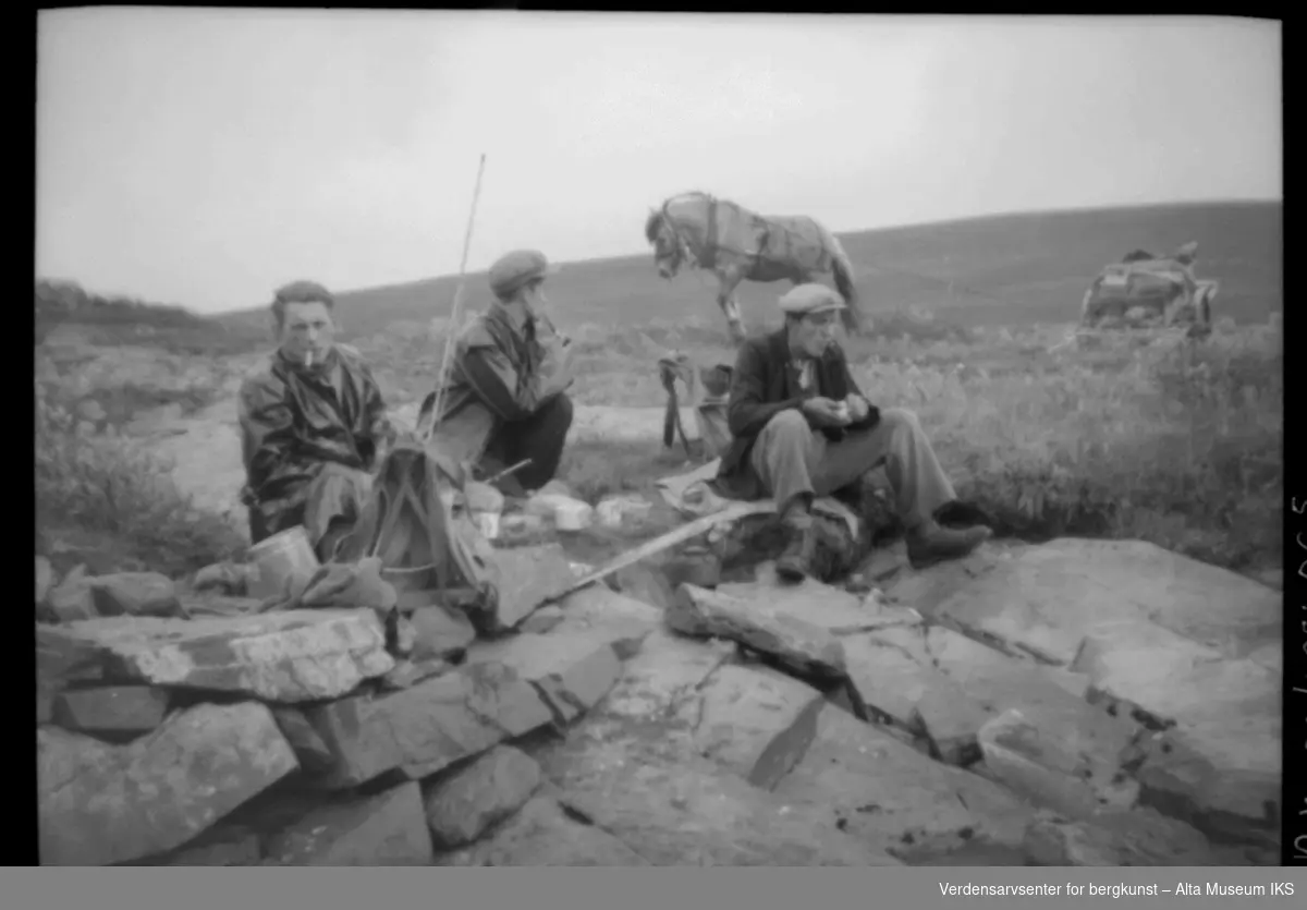 3 menn med fiskestang, hest og vogn slapper av ved noen steiner.