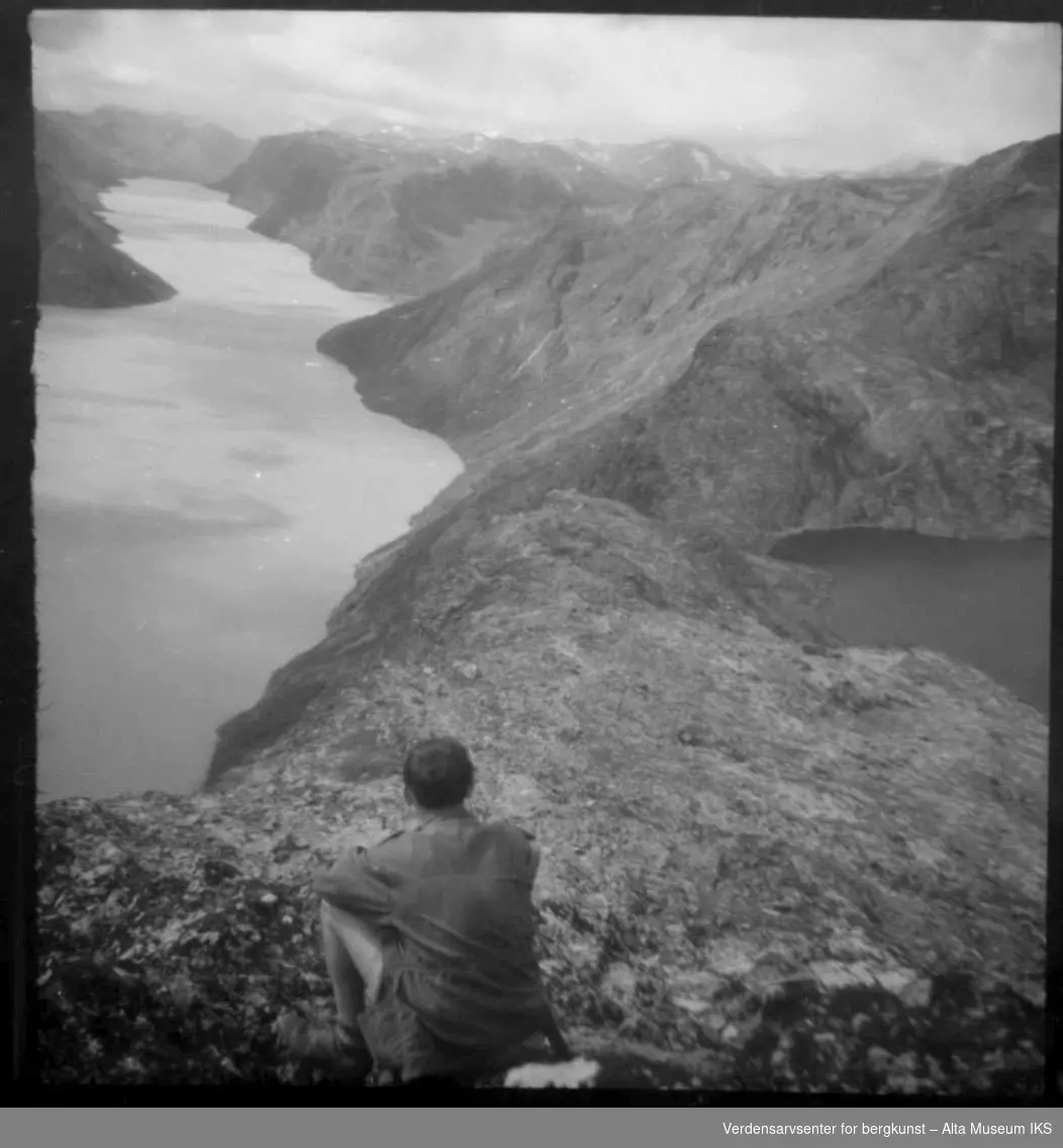 Mann sitter og ser utover fjell og innsjø.
