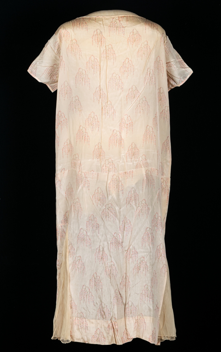 Klänning sydd i rak form med med insydda kilar av crepetyg.  Rosa botten med stiliserade tårpilar som motiv.