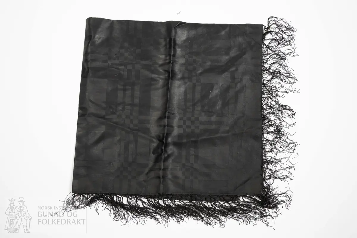 Tørkle av svart silke.
Rutemønster danna av sateng og lerret.
Moirèbehandla. Med påknytta frynser.