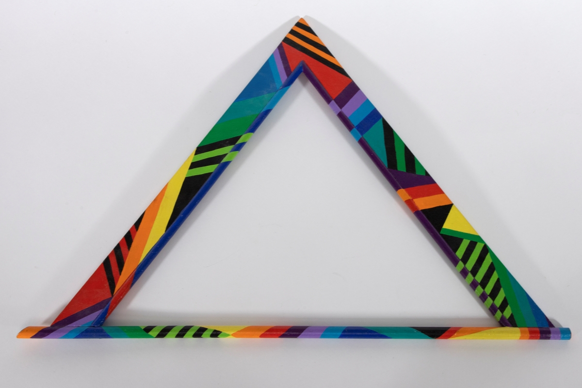 Skulpturelt halssmykke i trekantform satt sammen av en treplate og trepinner. Treelementene er malt i flere farger i geometriske mønstre. Smykket tres over hodet.