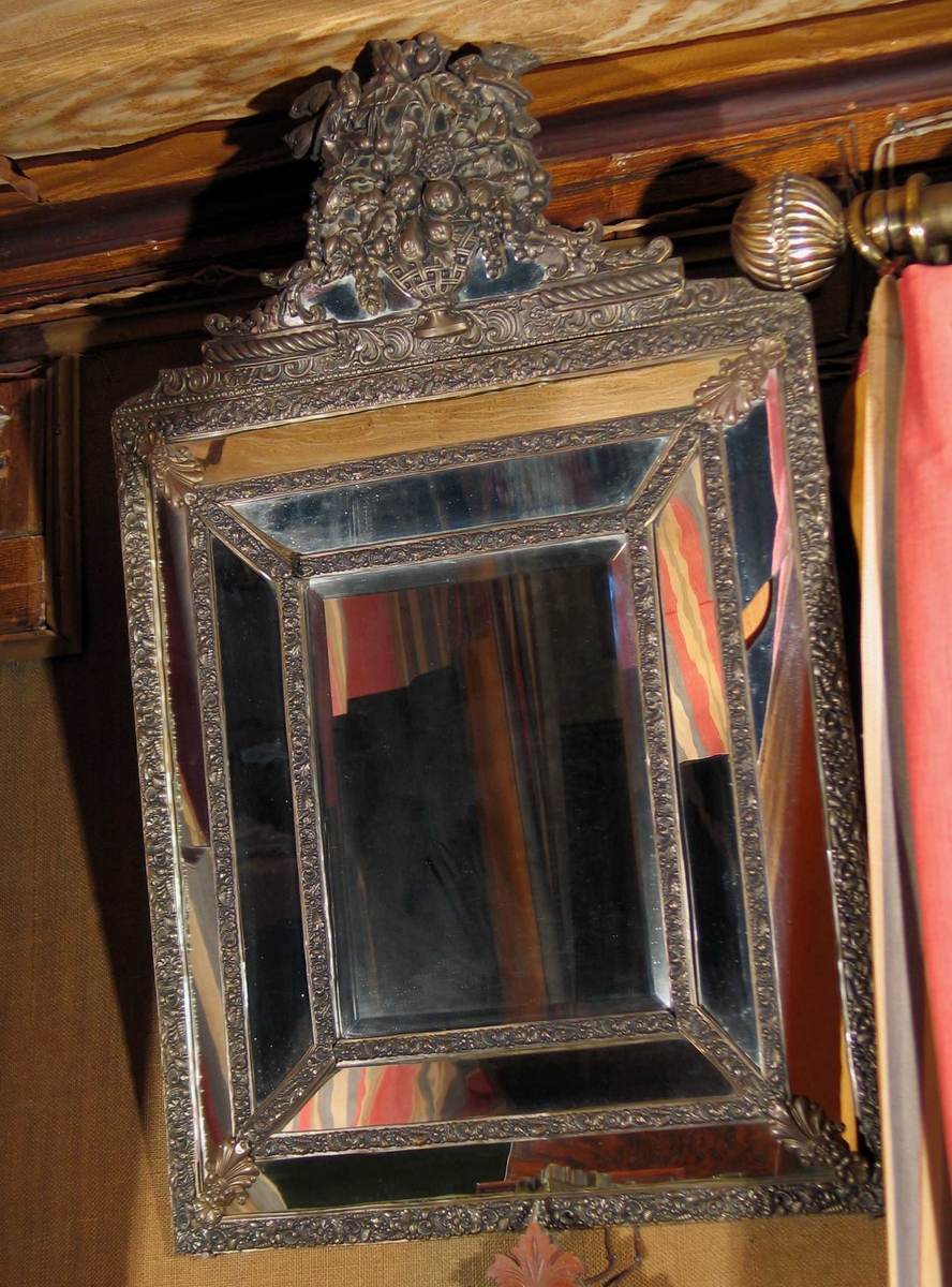 Speil med skrå felter på siden og over. Slipt glass i midten. Hele rammeverket er dekorert i bronse med blomster og ranker i relieff. Øverst en blomsterkurv og speilfelter.