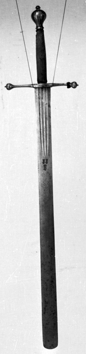 Skarprettersverd.  Pæreformet knapp med fasettetert dekor.
Tregrep viklet med rokkeskinn. 
Rette åttekantede parérstenger som ender i to dråper med kantet dekor. Rett tveegget klinge med ovalt tverrsnitt  og tre korte blodrender på hver side. Innslått tre smedstempler med kronede hoder.  På den ene siden er det gravert inn et hjul og på den andre siden en galge. Begge inngraveringer er innlagt med kobber.

