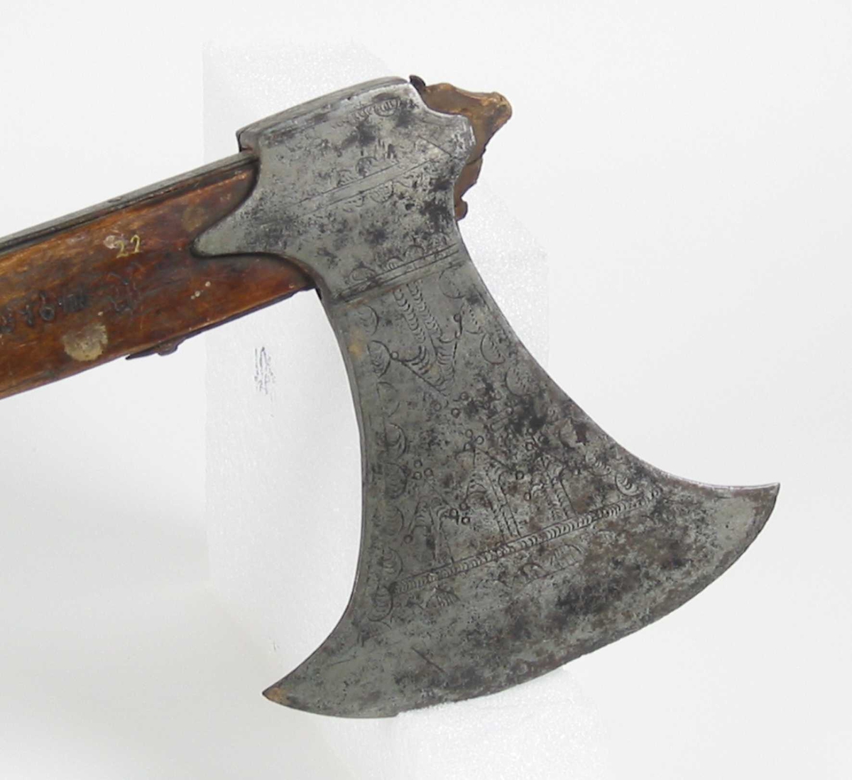 Symmetrisk blad. Bladet er tynt. 
Øsehammeren har skaftehull og fliker.
Etset dekor på begge sider. Stemplet TS på venstre side.
Gammelt treskaft med to orginale jernskinner med gravert dekor.
Jernskinnene er festet med nitter.