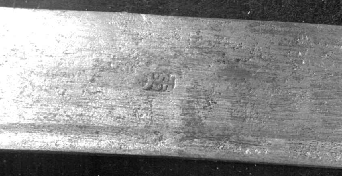 Rund tønneformet knapp i tre. Asymmetrisk feste med tre sidebøyler som har fortykninger på midten på utsiden og tommelbøyle og to sidebøyler på innsiden. Nyreformede parérplater. S-formede runde parérstenger med fortykkede avslutninger på endene. Fremre parérstang er nyere.
Tregrep med jerntrådvikling.
Enegget krum kline med smal ryggstillt blodrand. Smedmerke på venstre side. Klingespissen er dekorert med tre små hull.