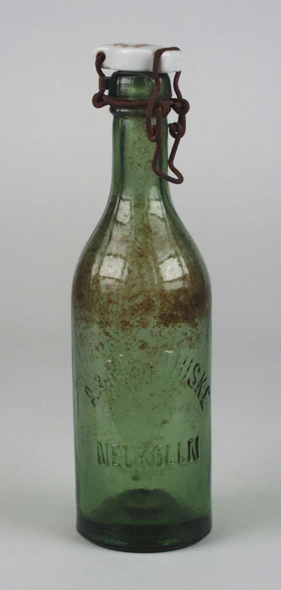 Grønn flaske med patentkork av hvit porselen. Korken mangler pakning og ståltråden er rusten. Rødt produsentstempel på toppen.