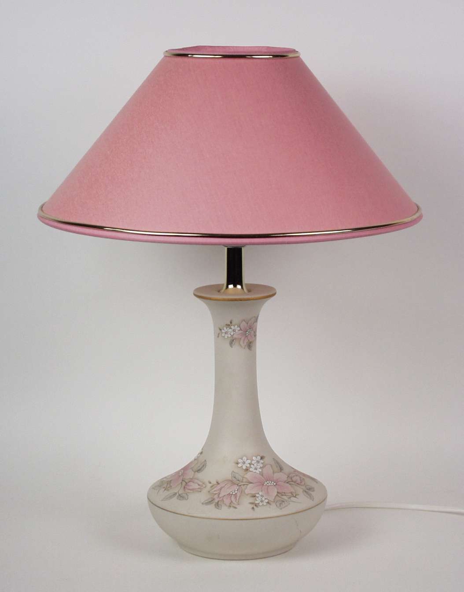 Hvit lampe i keramikk med pastellfarget blomstermotiv og rosa lampeskjerm med gullist.