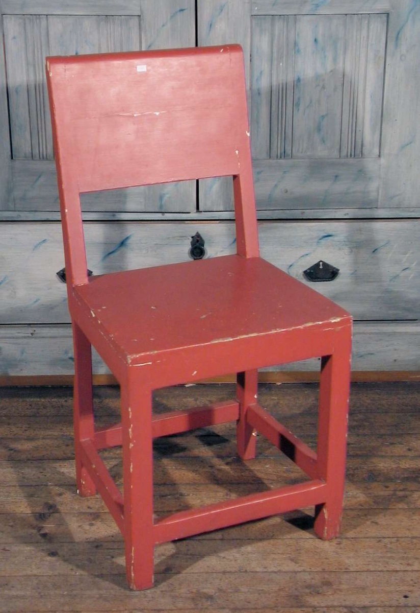 Rødmalt stol med tett rygg.