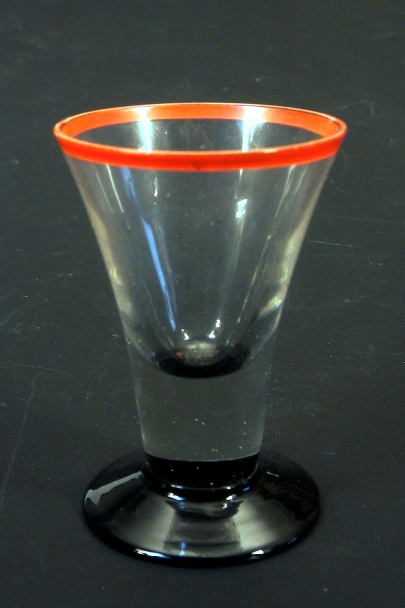 Drammeglass med sort fot og rød munningsrand.