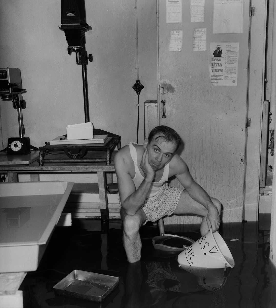 Fotograf Arne Gustafsson sitter i ett översvämmat mörkrummet på Studio Östgöta bild. 1967.
