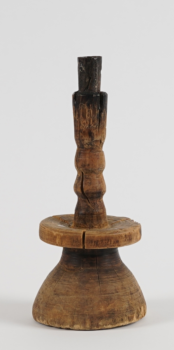 Form: Lysestake av tre med jarnpipe. Massingfasong med massiv "kvelva" fot og brei skål.
