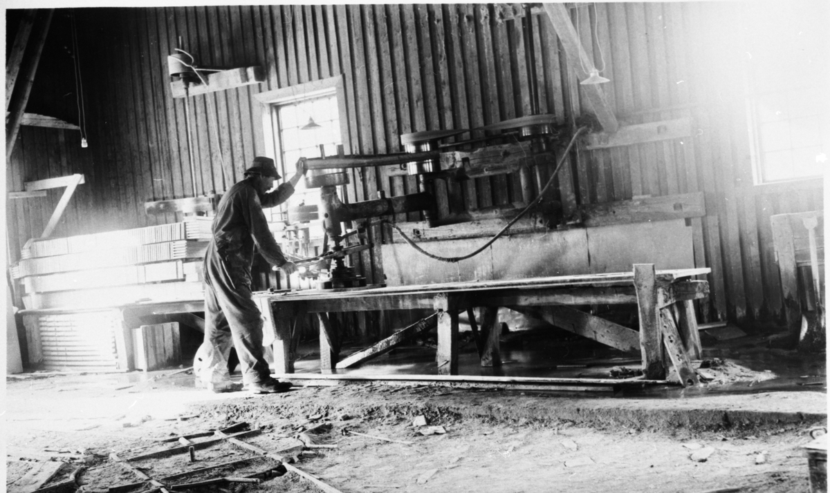 En mann står ved en maskin og arbeider ved Valdres Skiferbrud. Mannen er iført arbeidsklær og hatt.