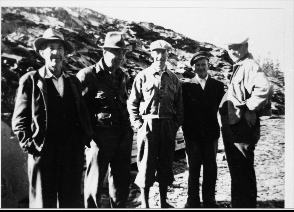 Fem menn fotografert foran en steintipp, sannynligvis i forbindelse med Valdres Skiferbrud. Alle mennene er iført hatt eller lue og en av mennene er iført en nikkers.