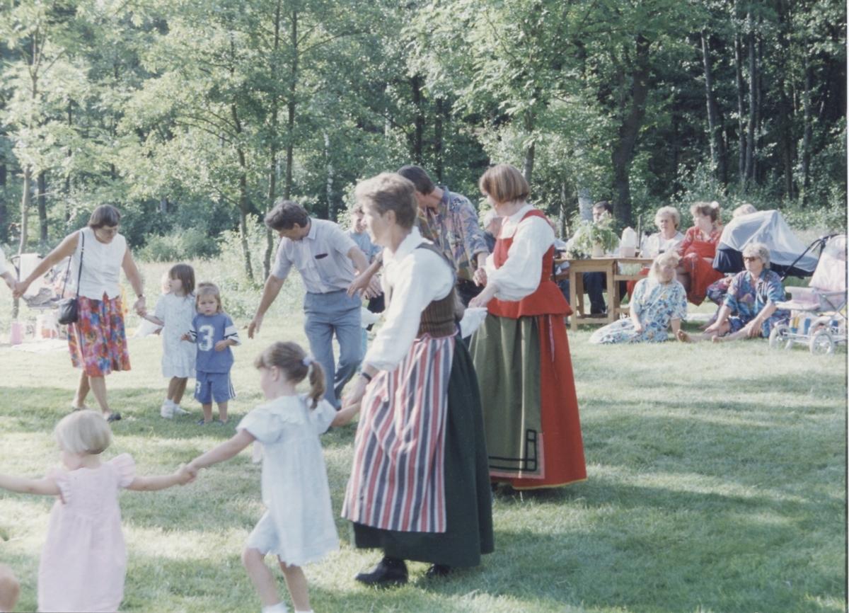 Midsommarfirande vid Hembygdsgården Långåker 1:3 1993. 
I folkdräkt med randigt förkläde dansar Karin Gustafsson (1933-2022). I röd folkdräkt Annika Bjerrhede. Övrigas namnuppgifter saknas.
Relaterade motiv: A03389 - A03408.