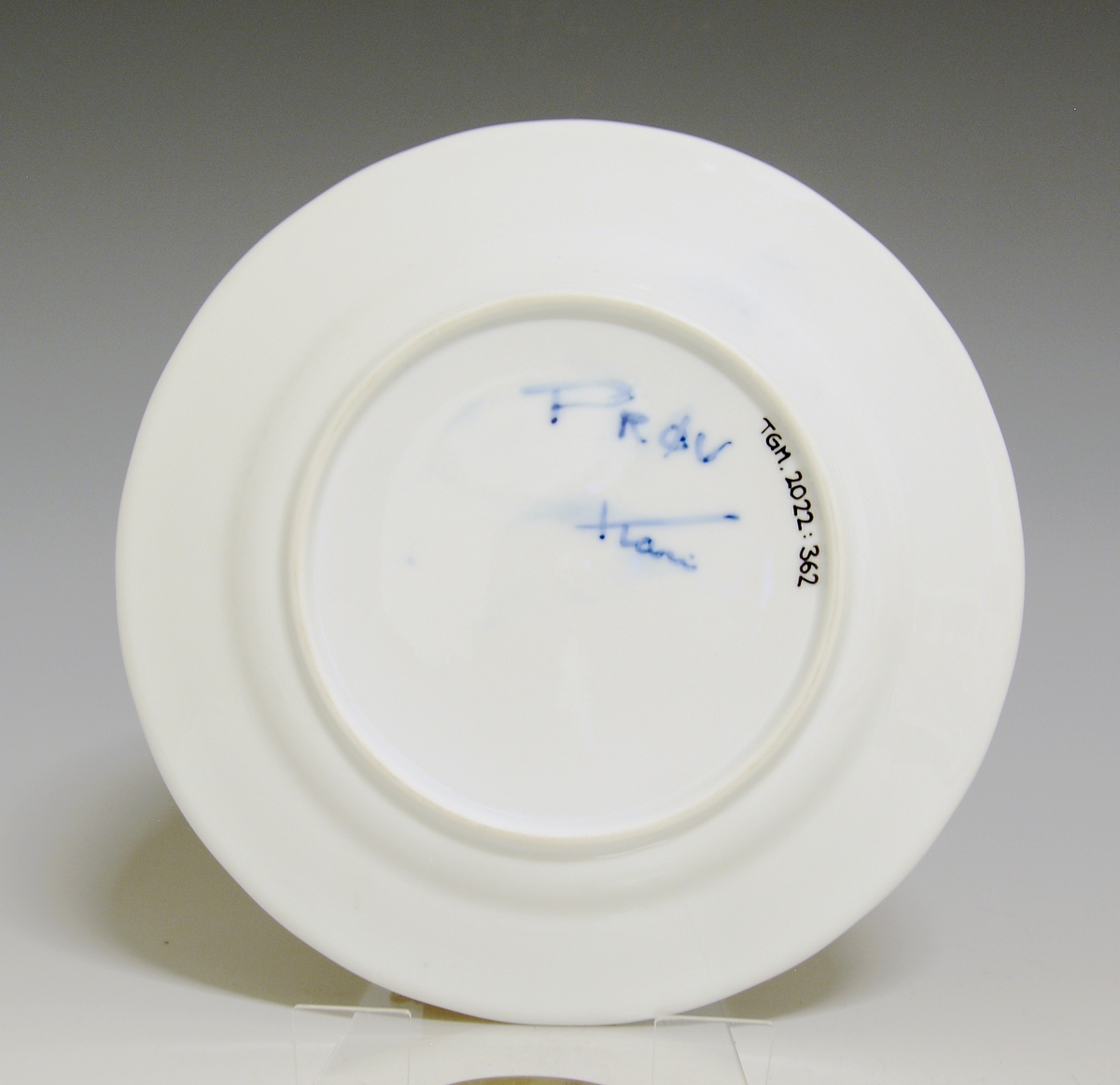 Liten tallerken av porselen. Hvit glasur. Håndmalt underglasurdekor i blått på fanen 
Modell: Victoria, 1800