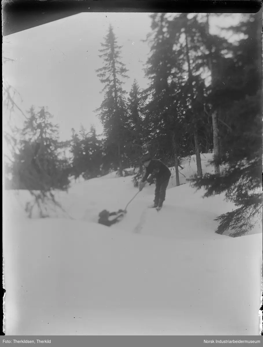 To menn i vinterlandskap. En av mennen holder en pinne ned til mann som står nedenfor en snøskavel.