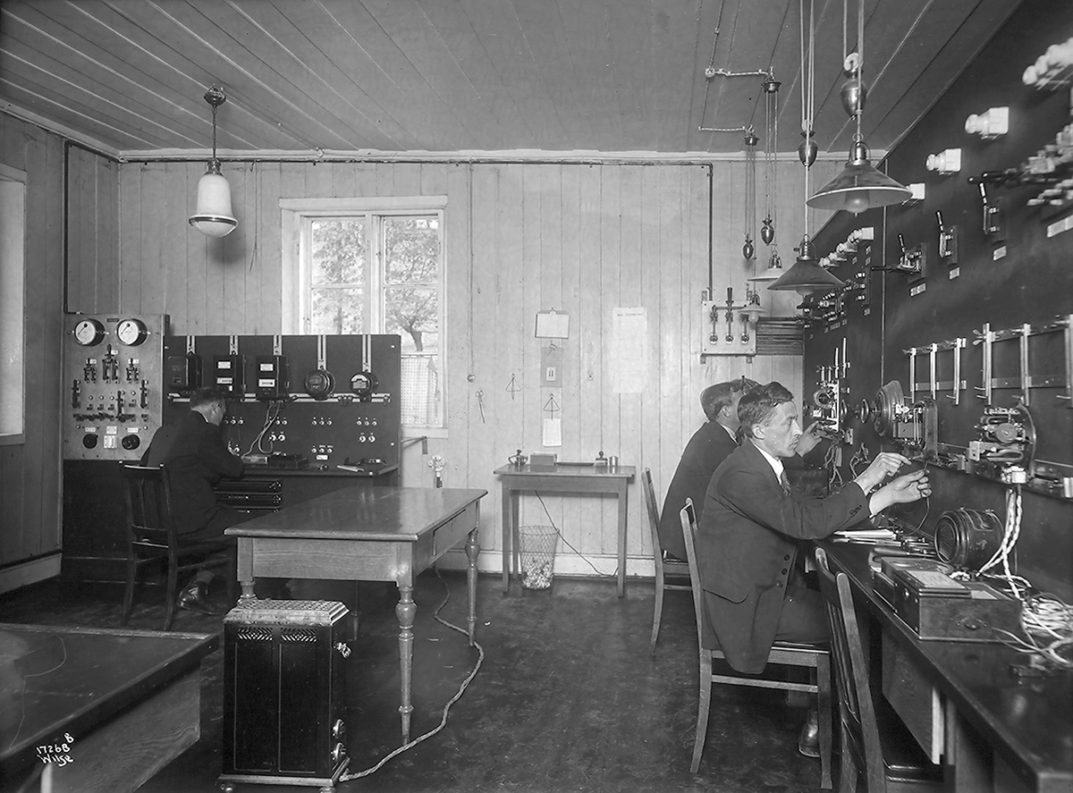 Tre menn sitter og styrer ledninger og instrumenter,  Elektrisitetsverket utstilling. Fotografert 1923.