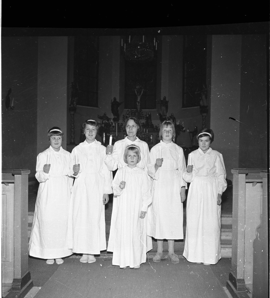 En luciakör står framför ett altare. De bär vita skrudar och håller i varsitt levande ljus.