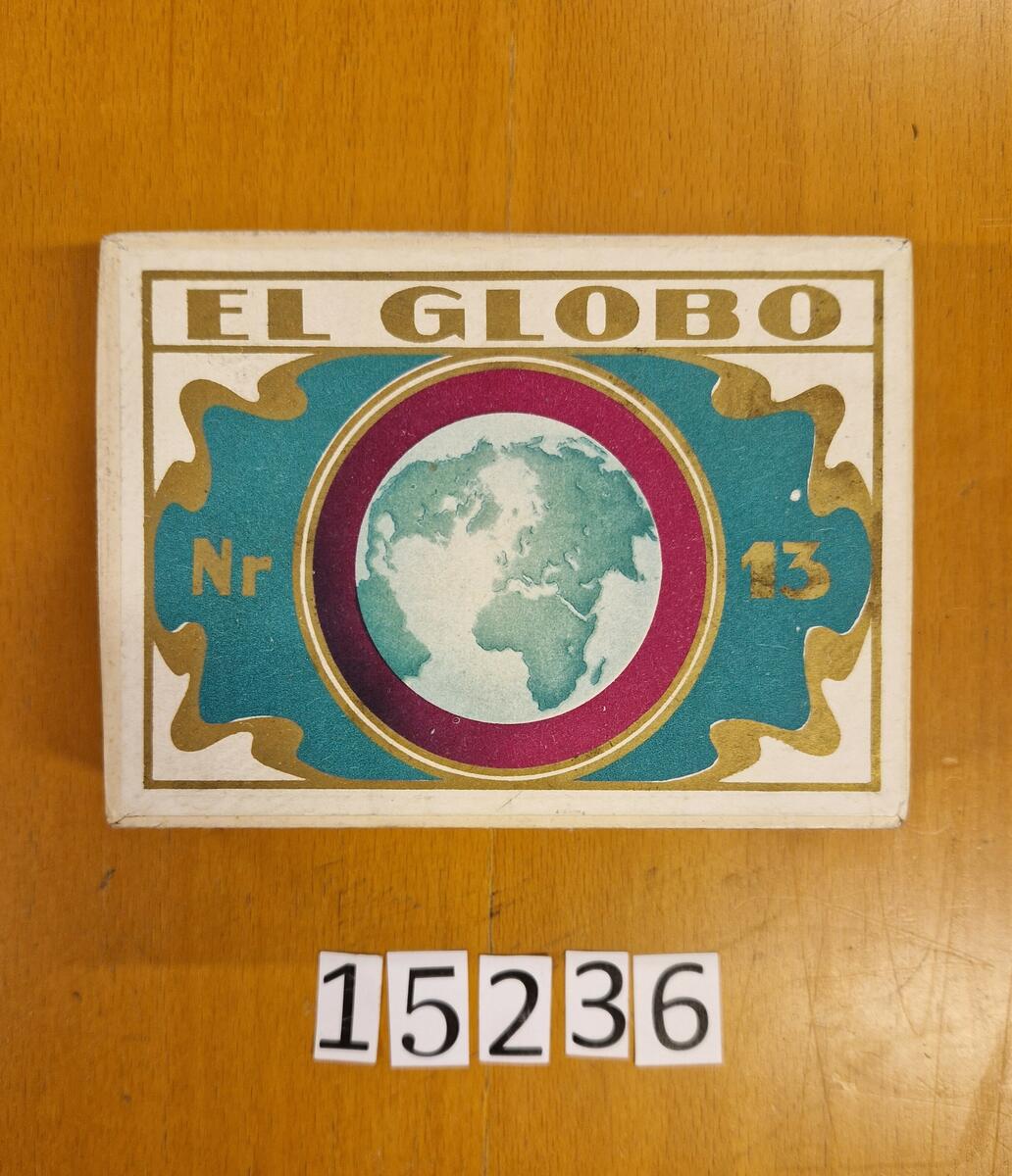 6 st cigarraskar "El Globo Nr 13". Etikett på långsidan. Pris per 1 st, 28 öre. Pris per 10 st, 2.80 kr. Kontrollstämpel Tobaksmonopolet. Gåva av Lena Eklöf Viklund, Sundsvall. Askarna innehåller pussel.

Anm: El Globo, N:r 13
Tillverkas av: Svenska Tobaksmonopolet (STA efter 1962, senare Swedish Match)
Svensk cigarr med lång historia. Tillverkades först av Unionen i Malmö. Tillverkades sedan av Förenade Svenska Tobaksfabriker, 1913-1915
Priset för 1 000 st år 1913 var 80 kr.

Svenska Tobaksmonopolet. Tillverkad:
1915-1916
1929-1934
1939-1940
1943-1959

Priset var 1915 11 kr för 100 st.
1929 var priset 15 öre per styck.
1940 var priset 10 kronor för låda om 50 st. samt 2 kronor för ask om 10 st.

 Källa: https://tobakshistoria.com/?portfolio=el-globo-nr-13
