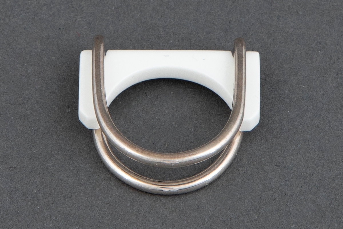 Ring bestående av et sølvbånd som er lagt dobbelt, bøyd i en dyp halvsirkelform og avrundet i begge ender. Det hører med fire utskiftbare deler av akryl. Disse er beregnet til å settes inn i sølvdelens åpne side, slik at det dannes en ring. Akryldelene er rett på den ene siden, konkav på den andre. 
De har fargene blank, hvit, blå og svart, slik at ringen kan brukes med forskjellig farge.