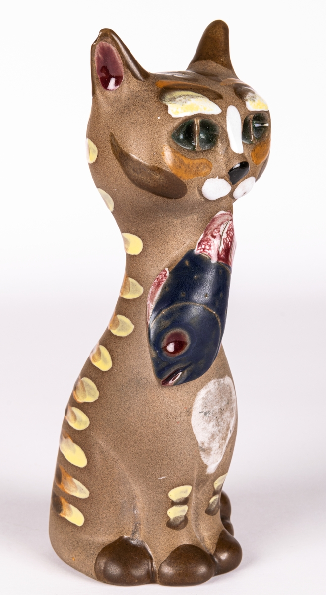 Figurin i form av katt med en liten fisk i munnen,  brunfärgat lergods med glaserade detaljer. Formgiven av Dorothy Clough för Gefle Porslin 1955.
