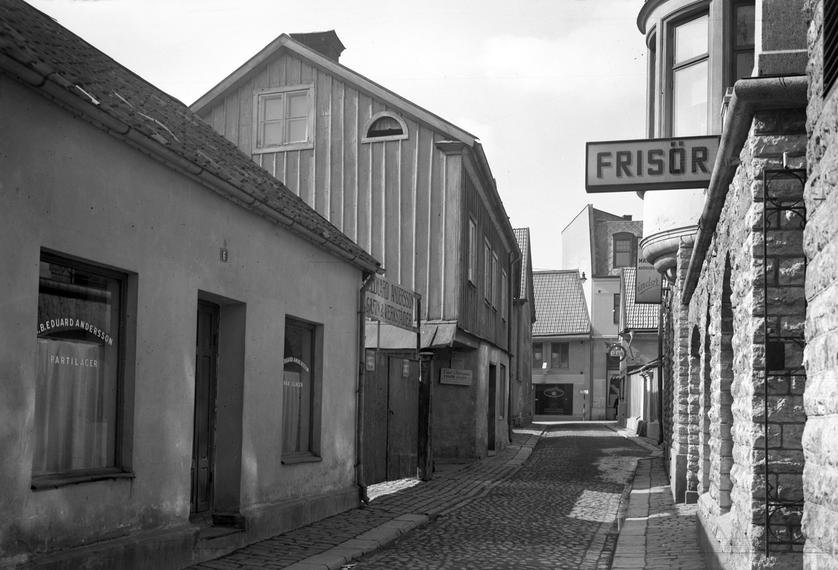 Miljön utmed Torggatan i Linköping har genomgått stor förändring sedan denna vy förevigades 1935. Byggnaderna till vänster är sedan länge rivna och platsen utlagd som torg. Trots det snäva perspektivet visar bilden något från tre välkända linköpingsföretag. Till vänster lagerlokalerna till Eduard Anderssons textilhandel på Storgatan, i fonden utmed Apotekaregatan skyltar Baumgardts pianomagasin och Hydén & Rundströms järnhandel.