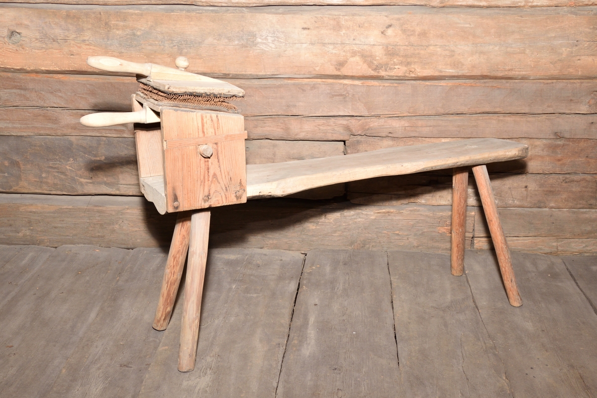 Kardstol med tillhörande kardor tillverkade i trä, kardorna med piggar i metall. Kardstolen med rektangulär kropp med indragen midja, på fyra enkla ben. I ena änden en ställning i trä för kardor, vilken kan skruvas åt. Kardorna med rektangulär form samt handtag. 