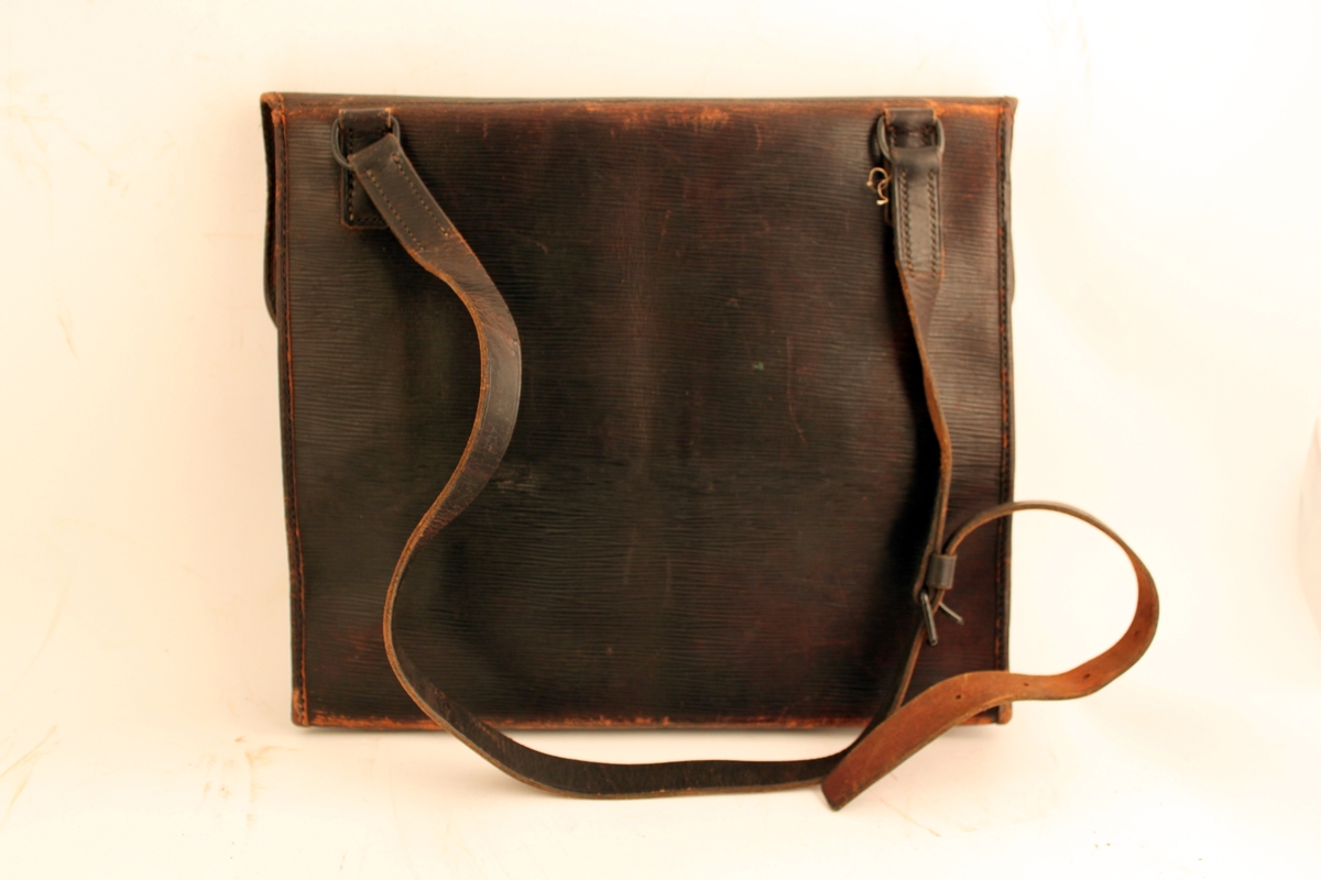 Väska av svärtat läder med axelrem och låsanordning med fastnitade järnöglor och låsten. Väskan försluts med hänglås (saknas). Klaff med förslutning med rem och hålspänne. Fyra hål på klaffen där en bricka varit fästad.